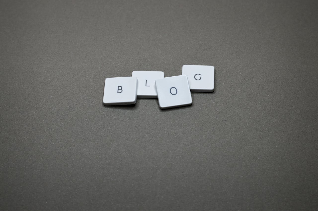 White Scrabble tiles spelling Blog against a minimalist gray background.